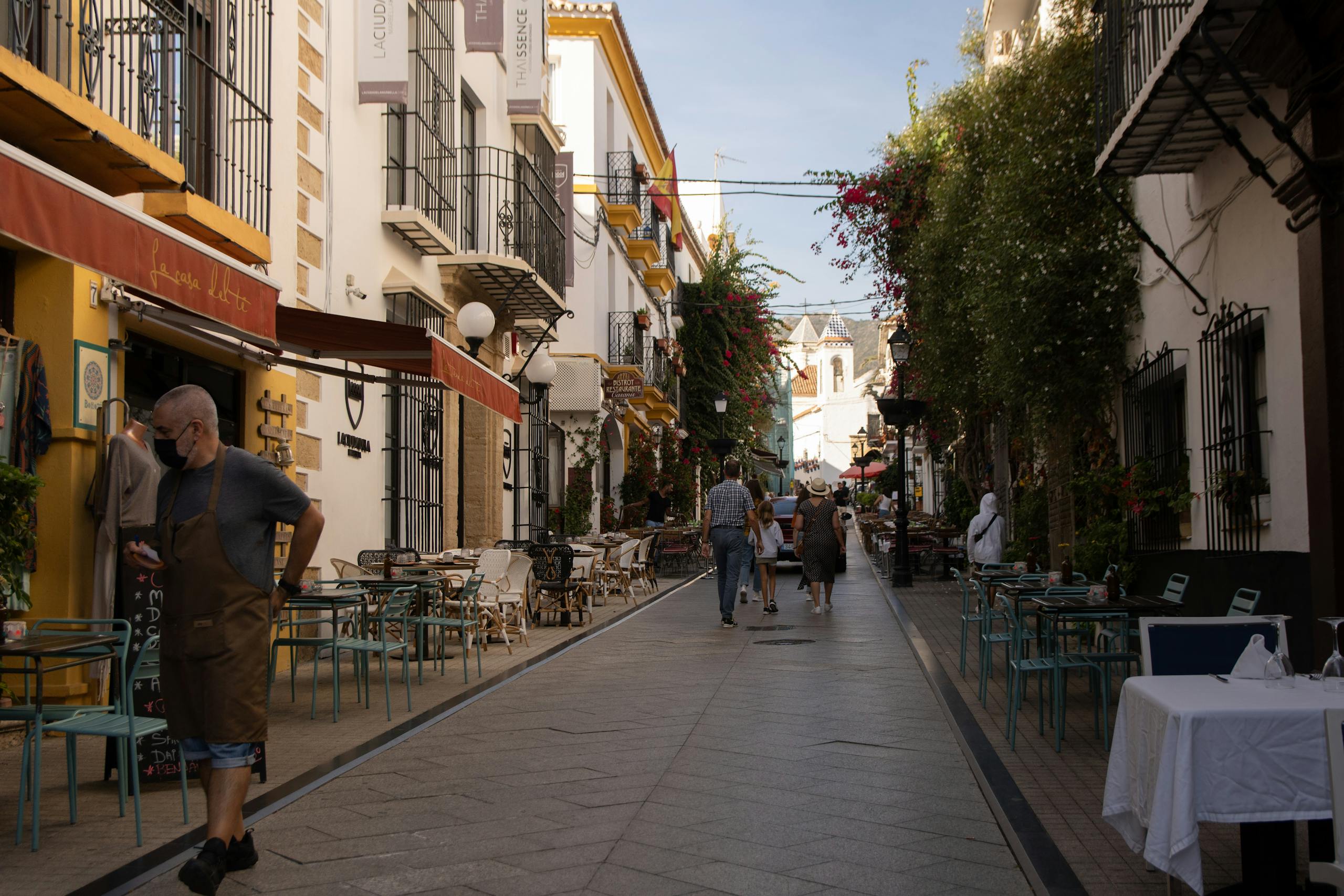 Stafford Affiliates Travel - A vibrant street in Marbella, Spain, with people walking past cafes and picturesque buildings.