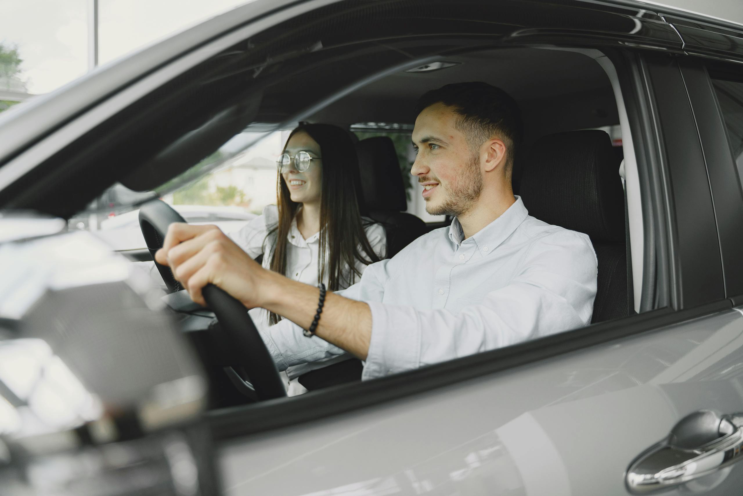 Stafford Affiliates Travel - A young couple smiling while driving together in a modern car interior.