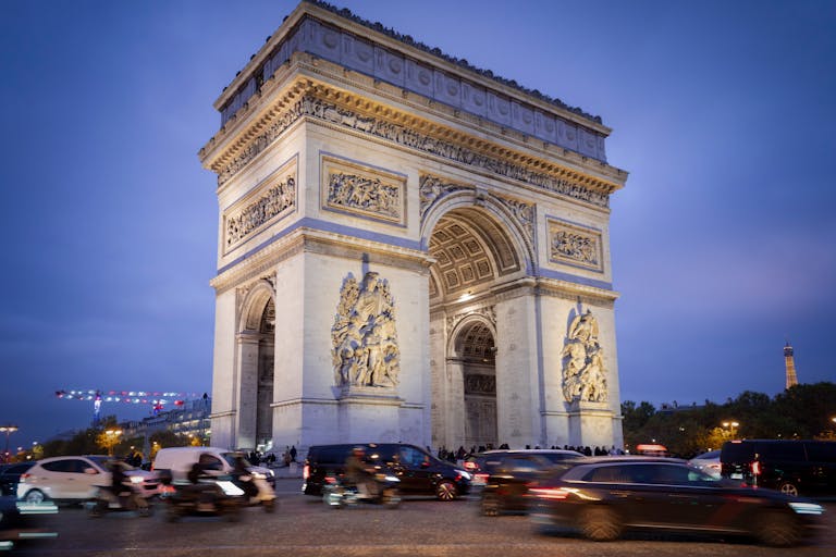 Stafford Affiliates Travel - Iconic Arc de Triomphe under blue evening sky with bustling traffic in Paris.