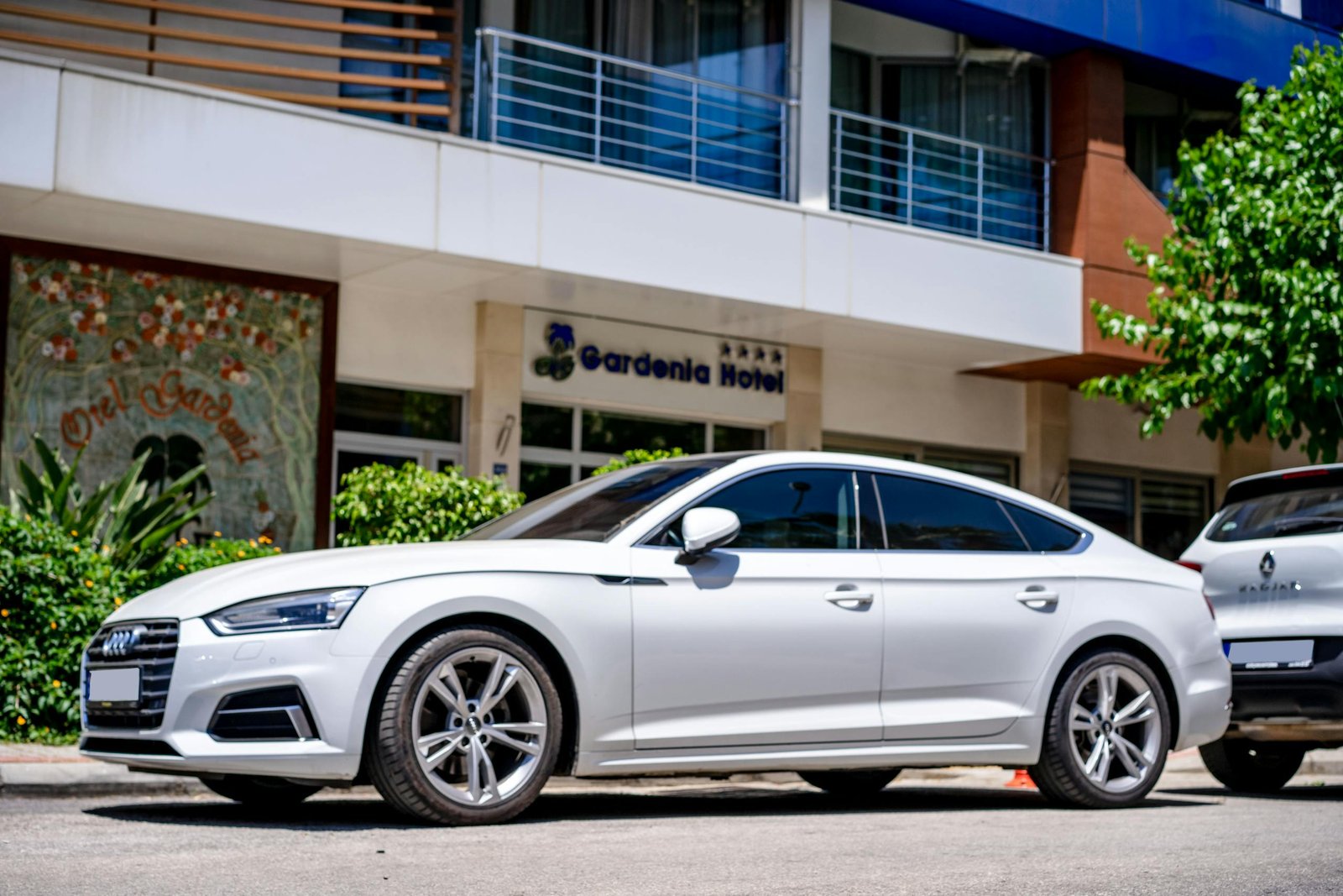 White luxury car parked in front of a hotel with modern architecture. Stafford Affiliates Travel