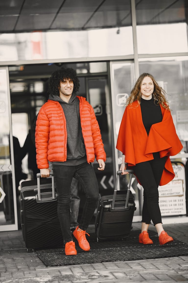 A cheerful couple exiting an airport terminal with luggage, dressed in matching red outfits - Stafford Affiliates Travel