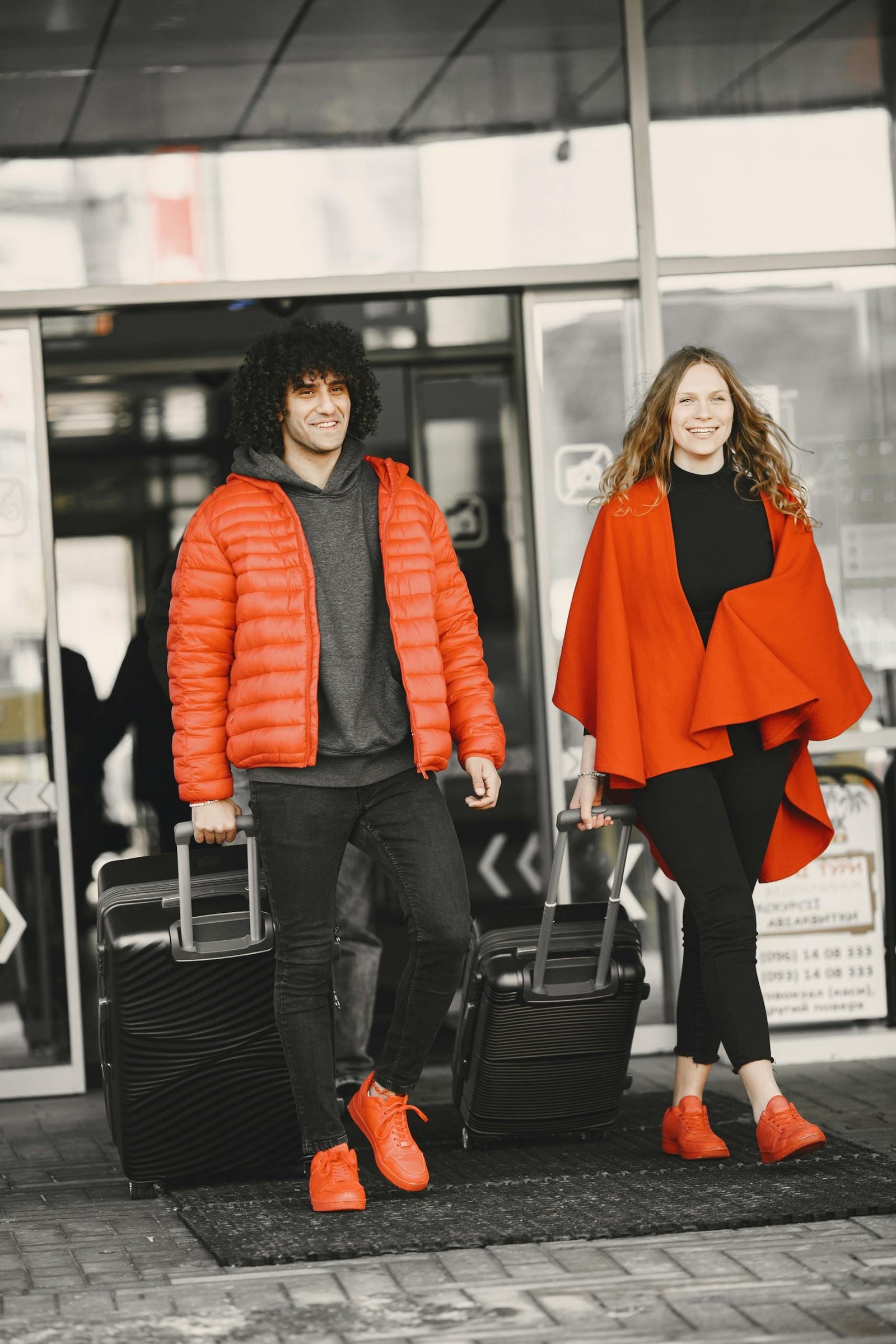 A cheerful couple exiting an airport terminal with luggage, dressed in matching red outfits - Stafford Affiliates Travel
