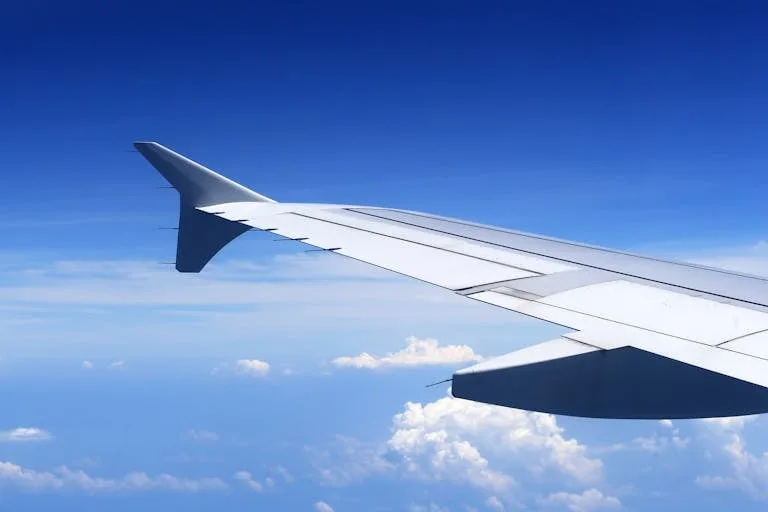 A stunning view from an airplane window showing a wing against a clear blue sky and clouds Stafford Affiliates Travel