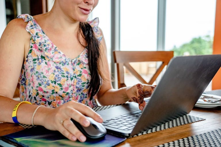 A woman using a laptop for booking a holiday, featuring a floral dress and henna design - Stafford Affiliates Travel