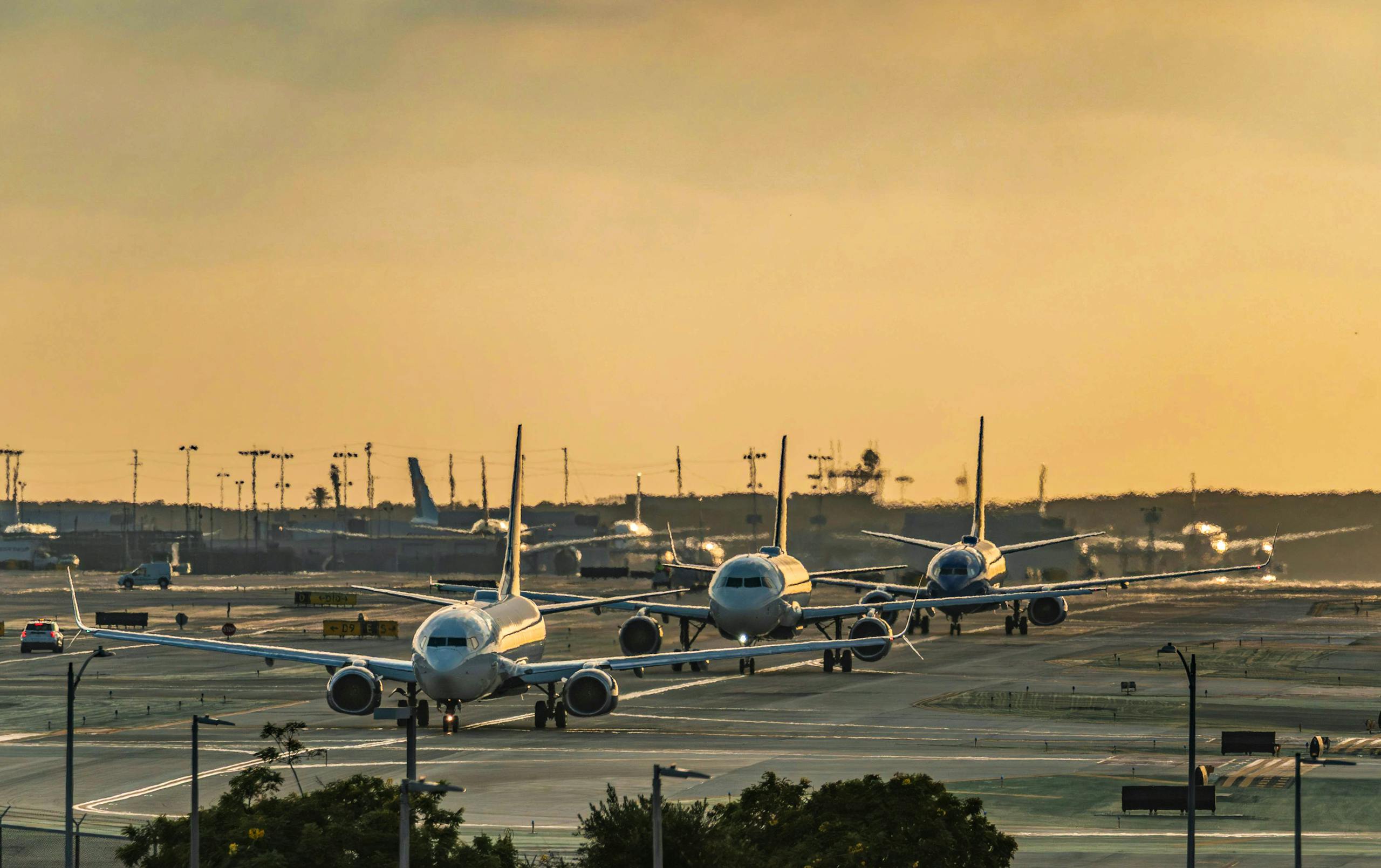 Multiple airplanes queue on a runway during sunset, creating a striking scene at a bustling airport Stafford Affiliates Travel