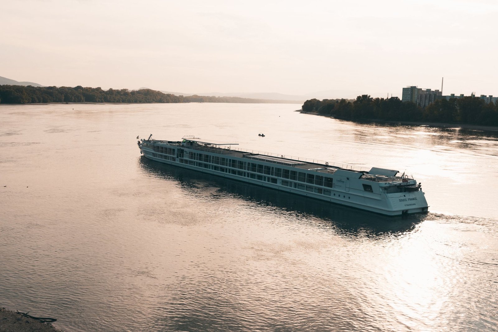 A scenic view of a cruise ship sailing on the serene Danube River near Estergon, Hungary - Stafford Affiliates Travel