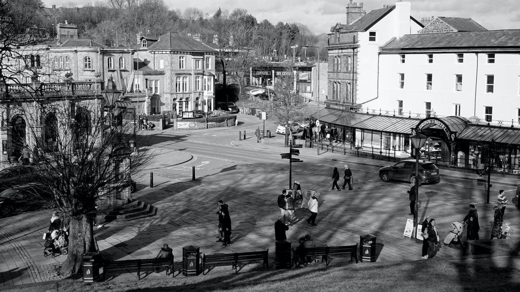 Black and white image of a busy street corner in Buxton, England, showcasing historical buildings and passersby - Stafford Affiliates Travel