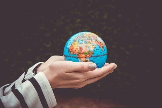 A person's hands carefully holding a small model globe against a dark blurred natural background, symbolising global ecotourism – Stafford Affiliates Travel.