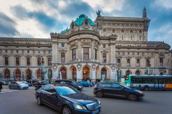 Vibrant scene of the Paris Opera House surrounded by moving traffic, showcasing classic architecture - Stafford Affiliates Travel