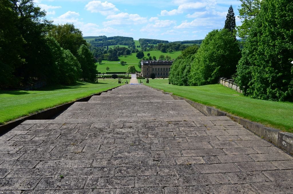 Wide angle view of Chatsworth House garden path, showcasing lush greenery and expansive landscape under a bright blue sky Stafford Affiliates Travel