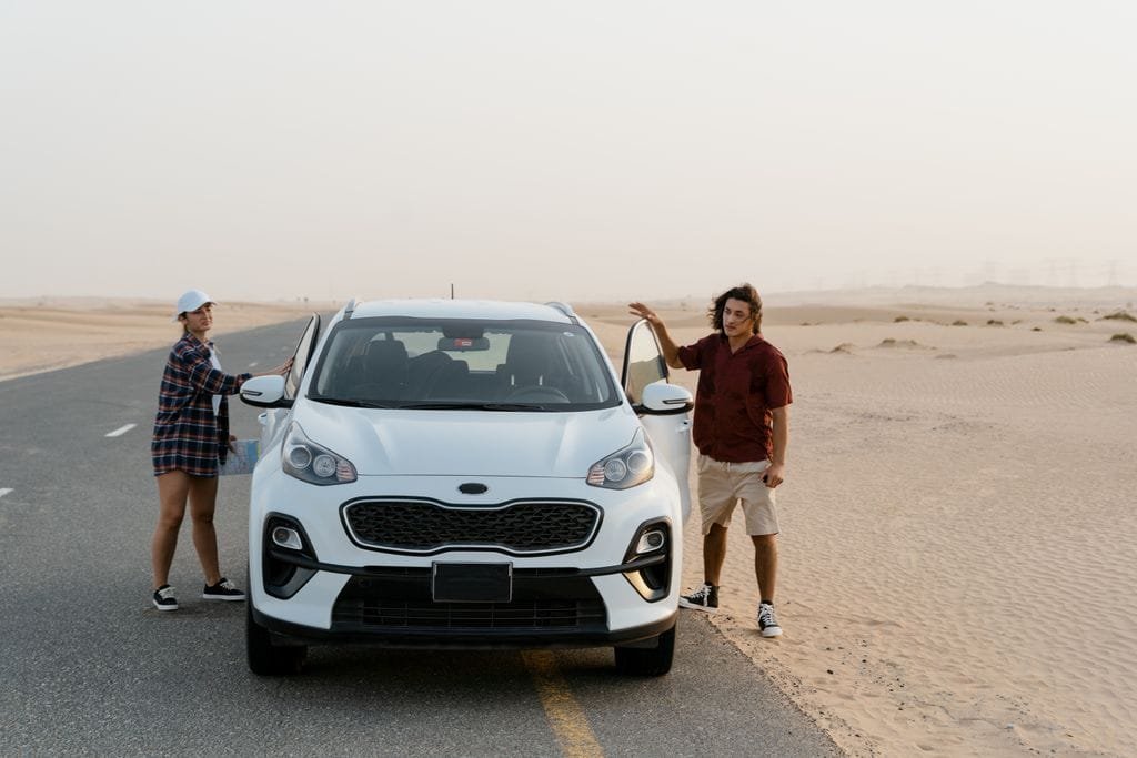 A couple stands by their SUV on a desert road, enjoying a scenic road trip - Stafford Affiliates Travel