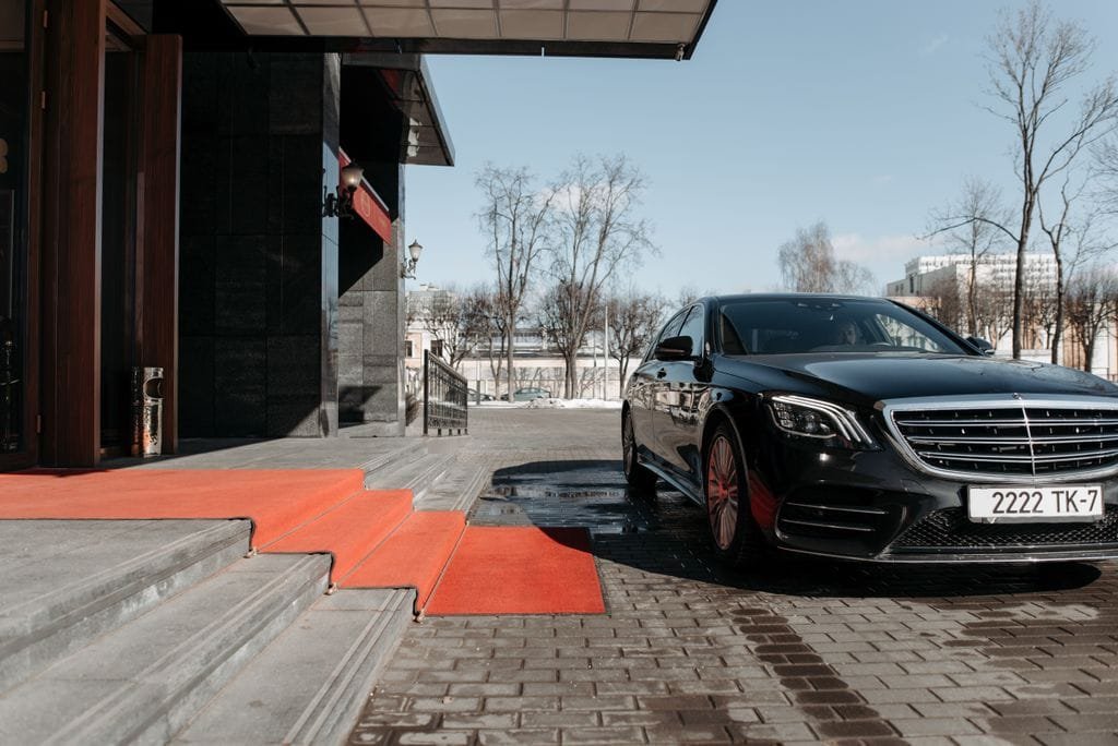 A luxury black sedan parked on a red carpet driveway outside a modern building Stafford Affiliates Travel