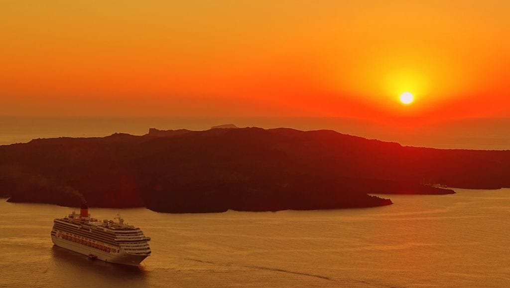 Captivating sunset over Santorini with a cruise ship navigating the calm sea. - Stafford Affiliates Travel