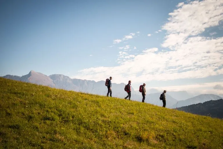 Four hikers with backpacks walking downhill on a sunny day with mountains in the background. HF Holidays Review: Complete UK Travel & Booking Guide / Stafford Affiliates Travel