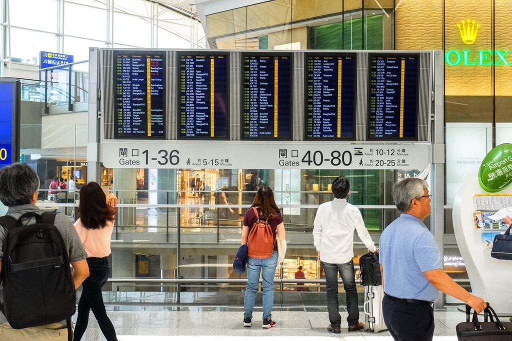 Passengers checking the departure board at Hong Kong International Airport terminal - Stafford Affiliates Travel