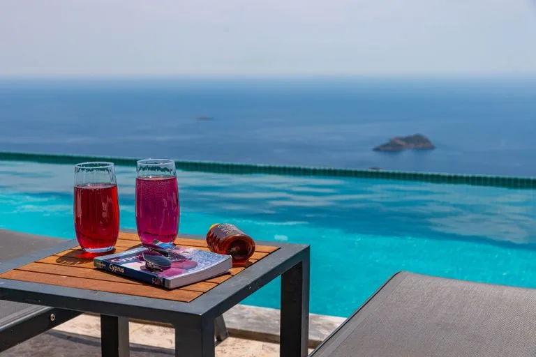 Serene poolside view with drinks, book, and infinity pool overlooking the sea. Booking.com Stafford Affiliates Travel