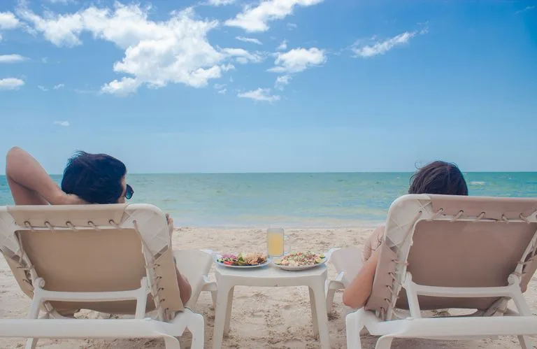 Two people relax on sunbeds with refreshments by the sea, enjoying a sunny summer day. eDreams UK Review: Flight Savings & eDreams Prime Guide / Stafford Affiliates Travel