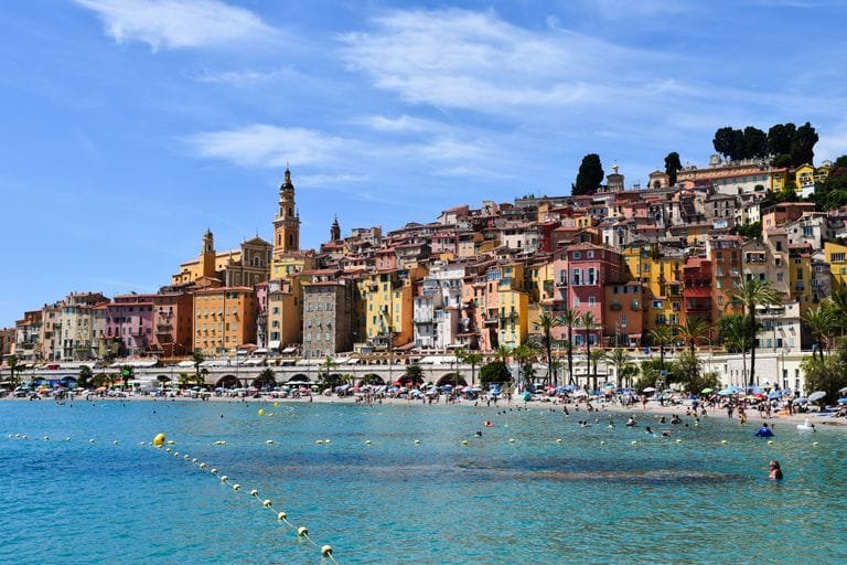 Vibrant beachfront scene in Menton, showcasing colorful buildings and lively summer activities. Hays Travel UK Review: Booking, Deals Guide / Stafford Affiliates Travel