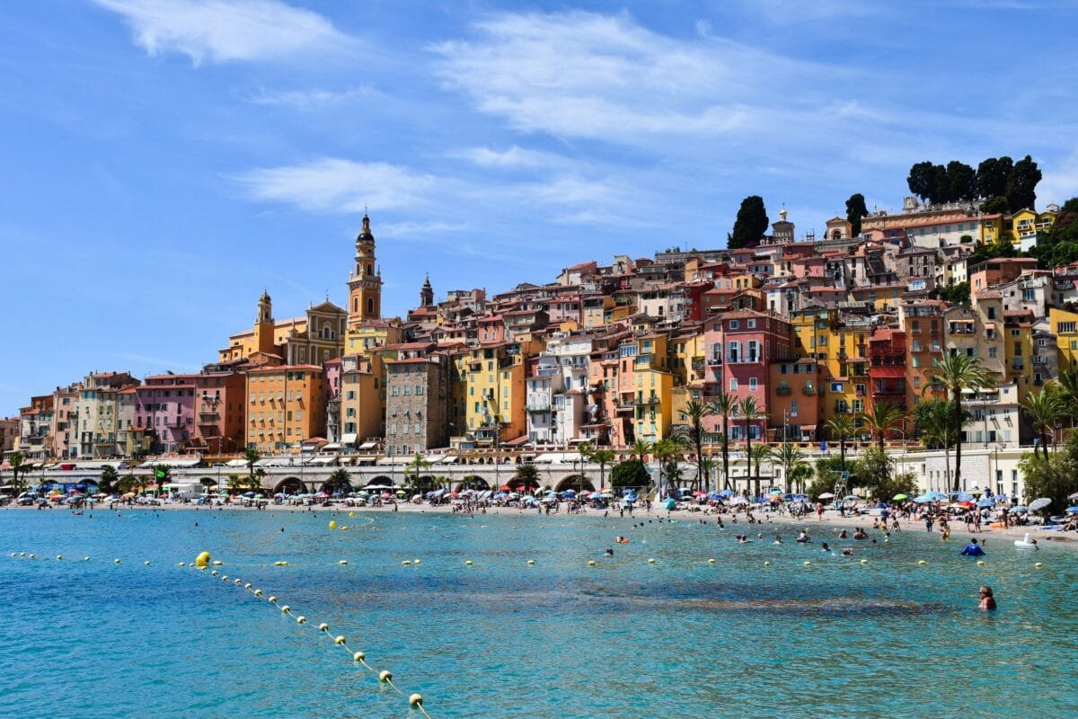 Vibrant beachfront scene in Menton, showcasing colorful buildings and lively summer activities. Hays Travel UK Review: Booking, Deals Guide / Stafford Affiliates Travel